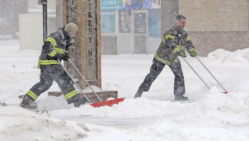 
              Mandan firefighters Shane Weltikol, left, and Chad Nicklos clear accumulating snow from outside the firehouse in downtown Mandan, N.D., as the Christmas Day blizzard intensifies on Sunday, Dec. 25, 2016. Most of the Dakotas and southwest Minnesota had turned into a slippery mess due to freezing rain Sunday morning before snow arrived later in the day as temperatures fell. (Tom Stromme/The Bismarck Tribune via AP)
            