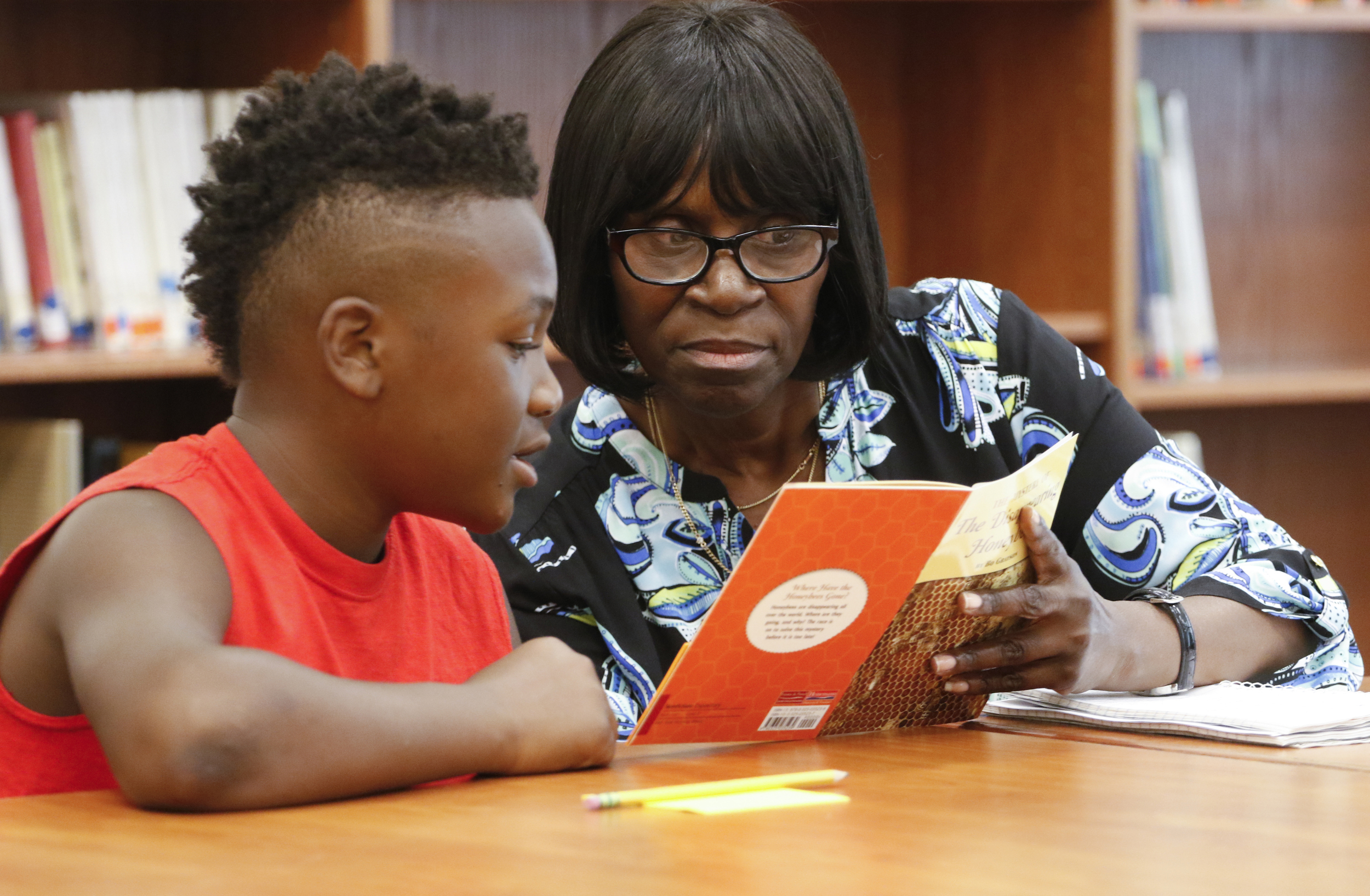 Fifth-grade student Cameron Tucker reads The Mystery of the Disappearing Honeybees with help from Orchard Knob Middle School Language Arts teacher Mae Pardlow during a literacy summit for educators at Orchard Knob Elementary School