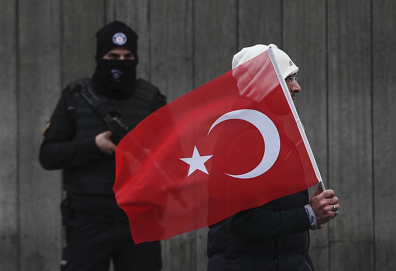 
              A man with a Turkish flag walks past a Turkish police officer guarding the scene, during a memorial outside the Reina club following the New Year's day attack, in Istanbul, Turkey, Tuesday, Jan. 3, 2017.  The Islamic State group claimed responsibility for the attack killing 39 people saying a “soldier of the caliphate” had carried out the mass shooting to avenge Turkish military operations against IS in northern Syria. (AP Photo/Emrah Gurel)
            