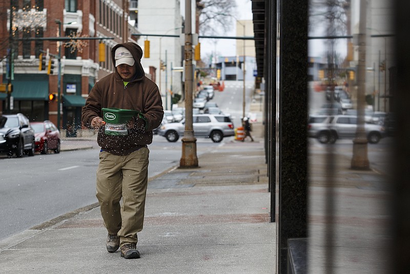 Carloz Ruiz spreads ice melter on the sidewalk around the First Tennessee building during sub-freezing daytime weather downtown on Friday, Jan. 6, 2017, in Chattanooga, Tenn. Temperatures are expected to remain below freezing for several days.