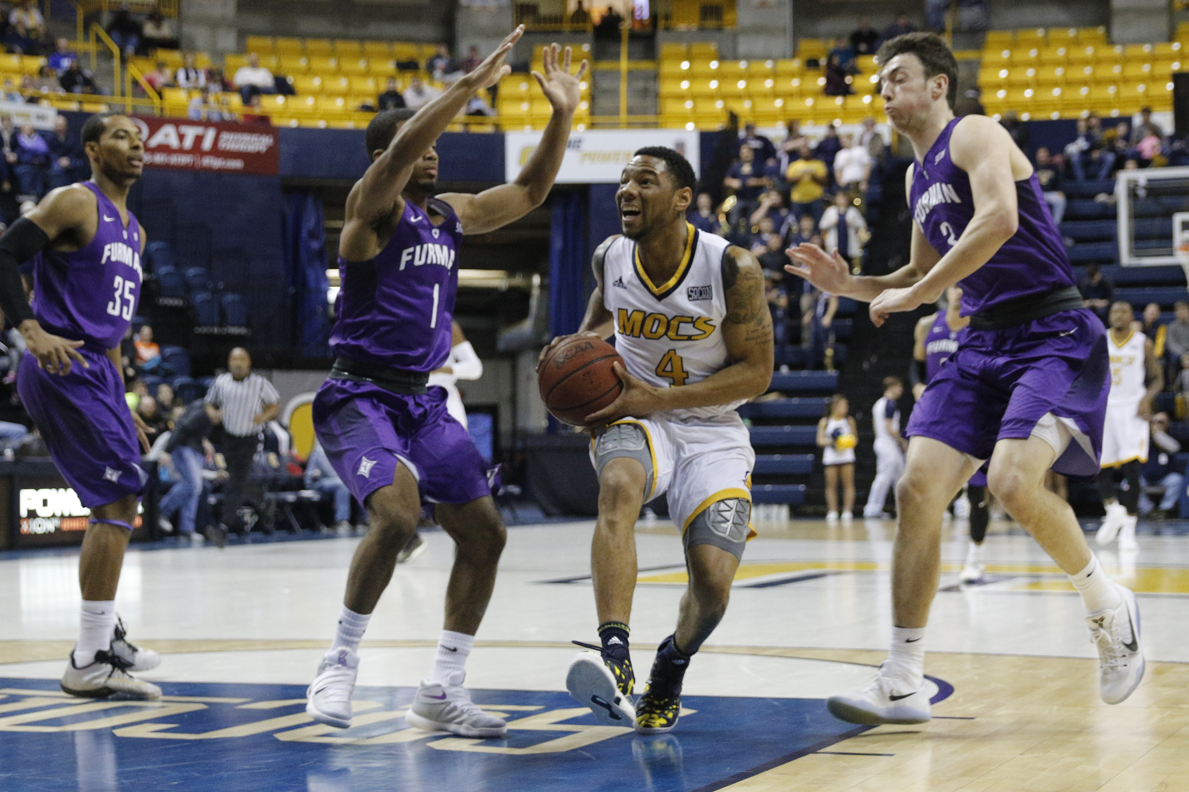 UTC senior guard Jonathan Burroughs-Cook cuts between Furman guard John Davis III, left, and forward Geoff Beans during Saturday's game at McKenzie Arena. The Mocs won the SoCon matchup 80-64.