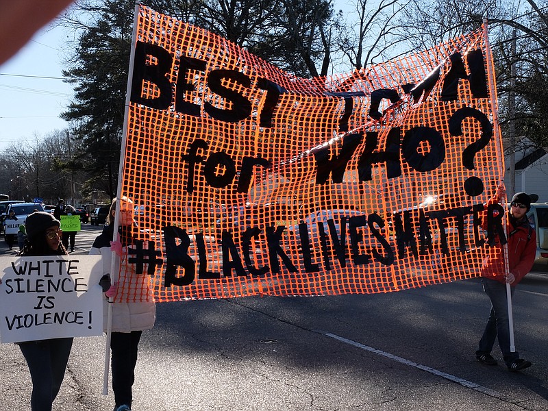 Bailey Allen, left, Madeleine Dougherty and Mark Gilliland, far right, carry signs on North Moore Road Monday during the annual M.L. King parade. 