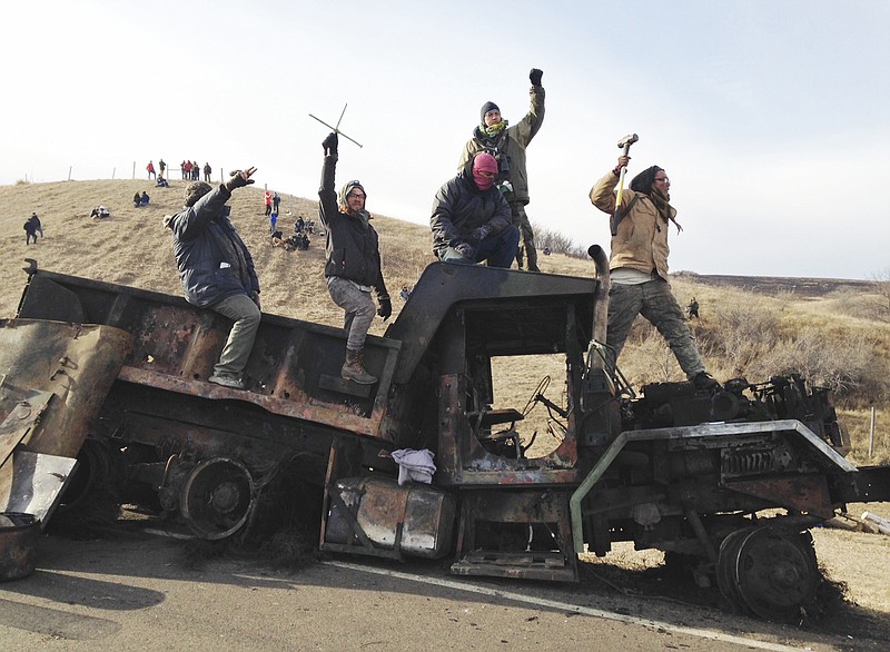 
              FILE - In this Monday, Nov. 21, 2016, file photo, protesters against the Dakota Access oil pipeline stand on a burned-out truck near Cannon Ball, N.D., that they removed from a long-closed bridge a day earlier on a state highway near their camp. Police allege in court filings that opponents of the oil pipeline made threats against officers and public officials in North Dakota last year, prompting additional security for the state's governor. The filings are part of a lawsuit filed in November by pipeline protesters who accuse police of excessive force in the Nov. 20 clash over a blockaded bridge. (AP Photo/James MacPherson, File)
            