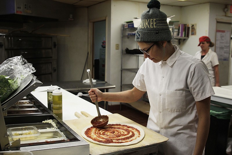 In this Jan. 9, 2017, photo, Andrea Ledesma spreads sauce on pizza dough at Classic Slice restaurant in Milwaukee. The 28-year-old has a four-year degree and quit a higher paying job because it made her miserable. Ledesma thought she would be making more at this point in her life and she's not alone. With a median household income of $40,581, millennials earn 20 percent less than boomers did at the same stage of life, despite being better educated, according to a new analysis of Federal Reserve data by the advocacy group Young Invincibles. (AP Photo/Carrie Antlfinger)