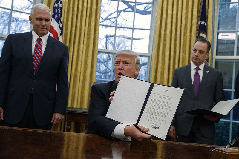 
              Vice President Mike Pence, left, and White House Chief of Staff Reince Priebus watch as President Donald Trump shows off an executive order to withdraw the U.S. from the 12-nation Trans-Pacific Partnership trade pact agreed to under the Obama administration, Monday, Jan. 23, 2017, in the Oval Office of the White House in Washington. (AP Photo/Evan Vucci)
            