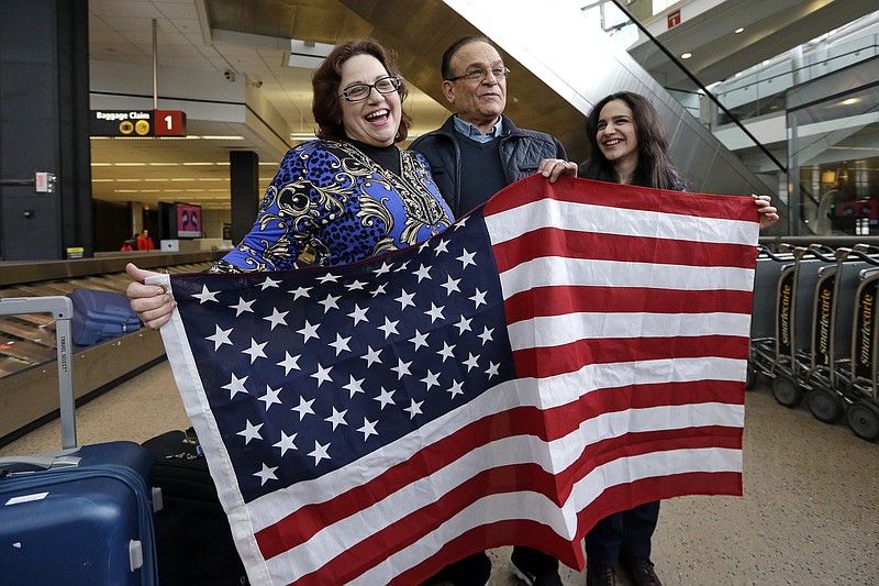 Jayne Novak, left, smiles as she stands with her husband, Allen Novak, newly-arrived from Iran, and their daughter Nikta, as they stand with a flag and pose for cameras Monday, Feb. 6, 2017, at Seattle Tacoma International Airport in SeaTac, Wash. Allen Novak joined his family, of Silverdale, Wash., on a conditional resident visa. Washington Governor Jay Inslee, Attorney General Bob Ferguson, and Port of Seattle Commissioner President Tom Albro joined family members Monday to welcome another immigrant, Isahaq Ahmed Rabi, who was blocked from entry last week due to President Donald Trump's immigration order. (AP Photo/Elaine Thompson)