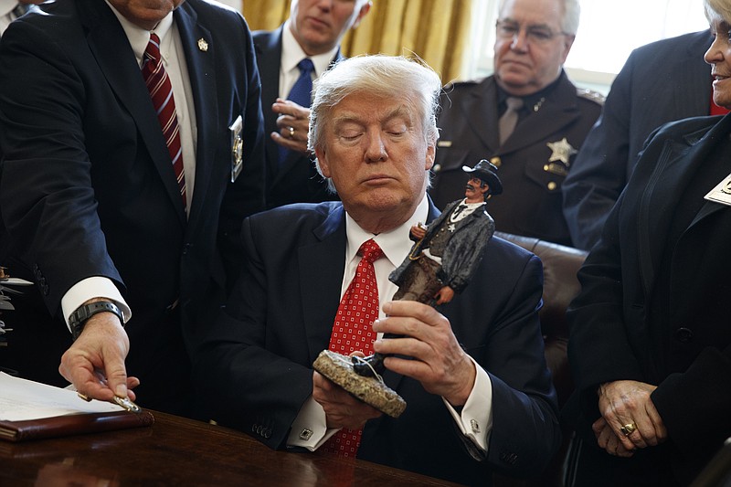 
              President Donald Trump looks at a figurine given to him by a group of county sheriffs, Tuesday, Feb. 7, 2017,  in the Oval Office of the White House in Washington. (AP Photo/Evan Vucci)
            