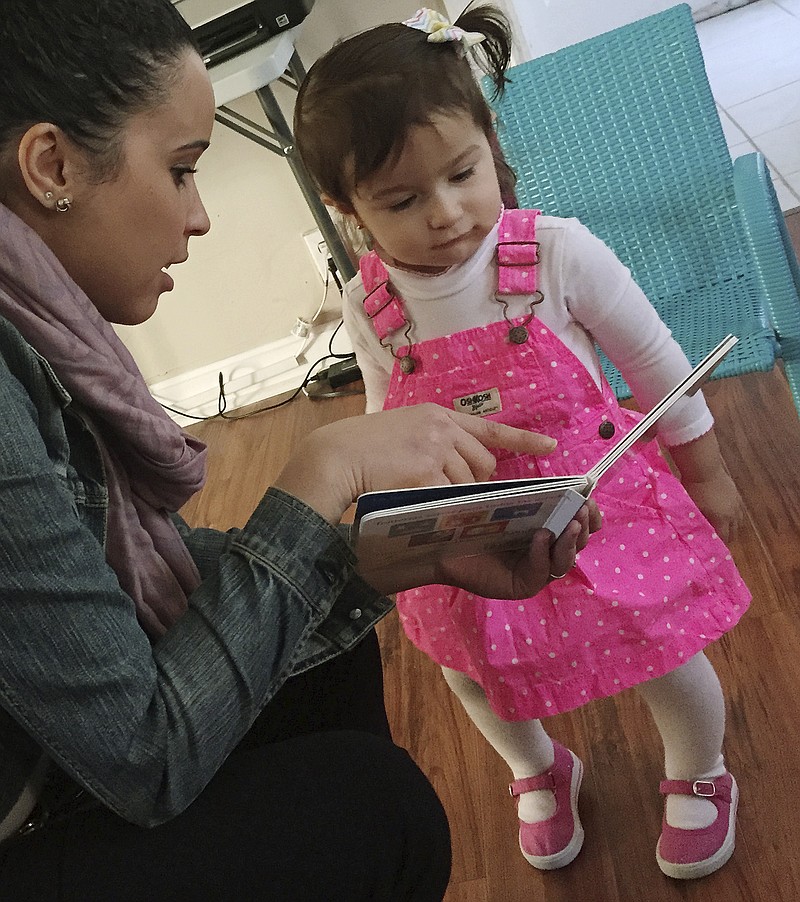 
              In this Jan. 11, 2016 photo, caseworker Stephanie Taveras, left, reads a book with 20-month-old Gracey Niebla, right, at the child's home in Providence, R.I. The city is in the third year of its effort to boost language skills for children from low-income families by equipping them with audio recorders that count every word they hear. During home visits, social workers go over the word counts with parents and suggest tips to boost children's language skills. (AP Photo/Matt O'Brien)
            