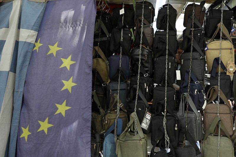 
              A man checks bags at a kiosk behind a Greek and an European Union flag at a market area in Athens, Monday, Feb. 20, 2017. Greece remains dependent on bailout loans from its partners in the eurozone to pay its debts and protect it from bankruptcy and a potential exit from the euro.(AP Photo/Thanassis Stavrakis)
            