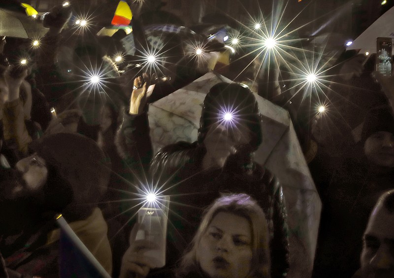 
              Protesters shine lights of their mobile phones while singing the national anthem outside the government headquarters in the rain in Bucharest, Romania, Sunday, Feb. 19, 2017. Braving the bad weather thousands gathered for the twentieth consecutive day to demand the government's resignation after it passed a decree, since withdrawn, that would have softened the corruption fight that has targeted top officials. (AP Photo/Vadim Ghirda)
            