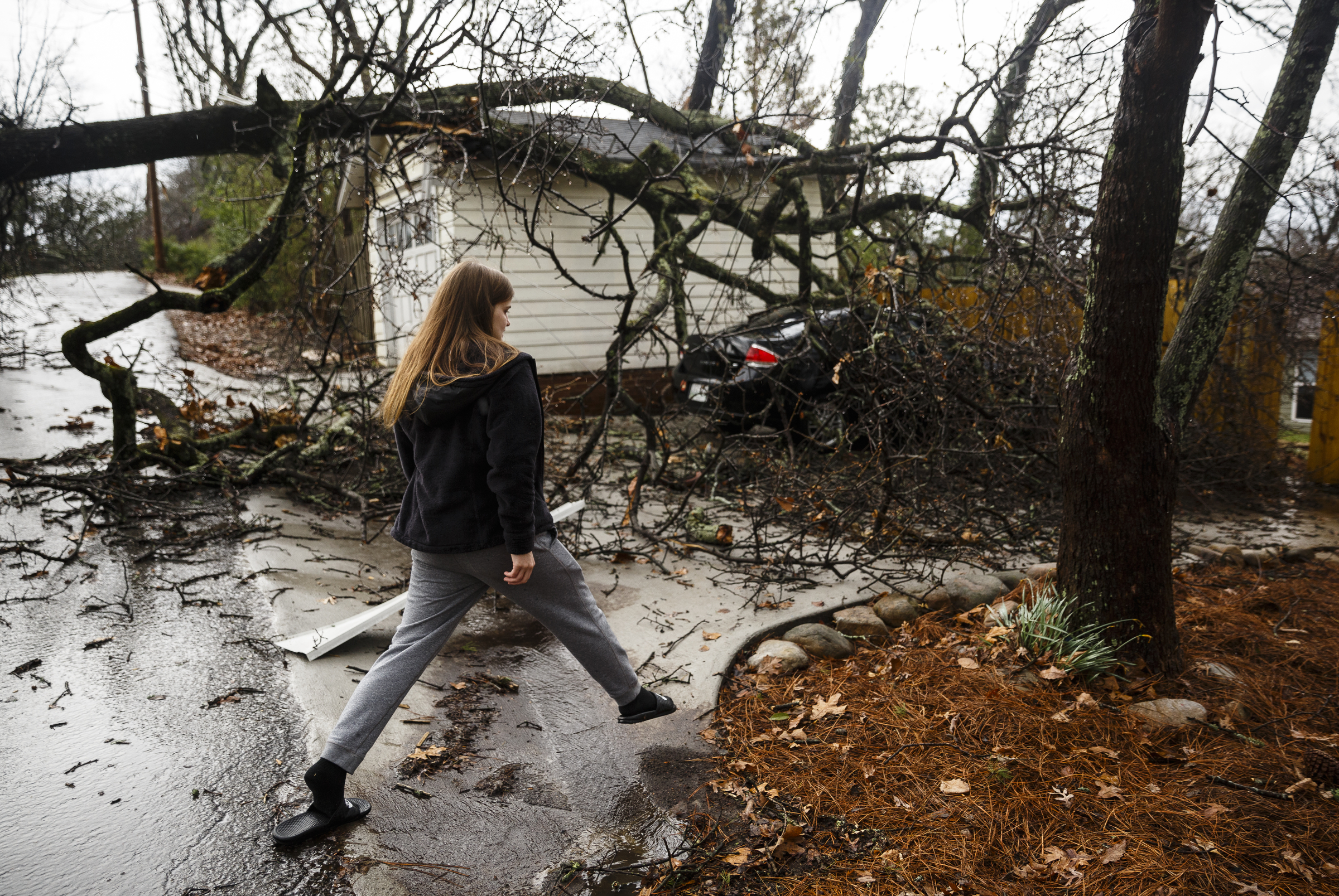 Baylee Fann crosses running water to check out damage from a downed tree that fell on her car outside a home between Westwood Avenue and Highland Drive on Wednesday, March 1, 2017, in Chattanooga, Tenn. Severe storms swept through the region Wednesday afternoon.