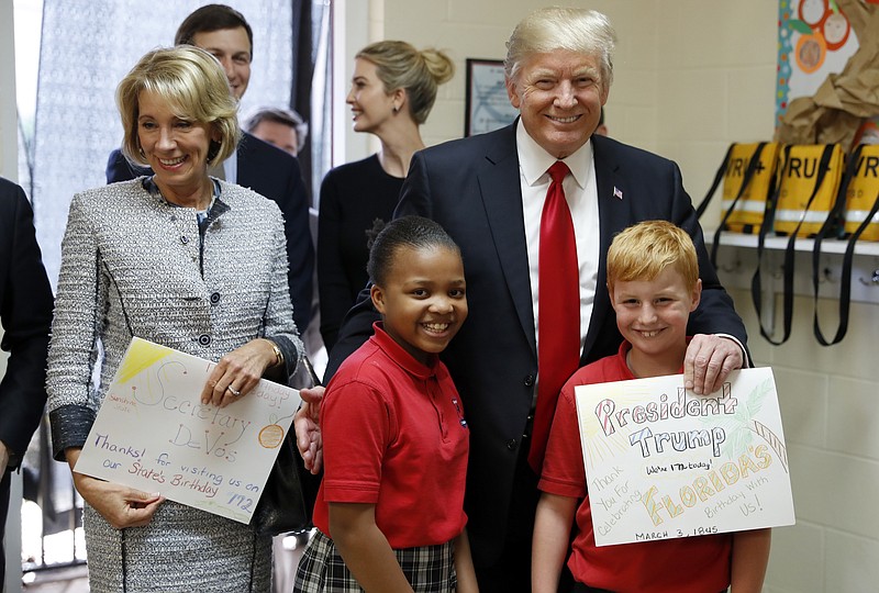 
              President Donald Trump and Education Secretary Betsy DeVos pose with fourth graders Janayah Chatelier, 10, left, Landon Fritz, 10, after they received cards from the children, during a tour of Saint Andrew Catholic School, Friday, March 3, 2017, in Orlando, Fla. (AP Photo/Alex Brandon)
            