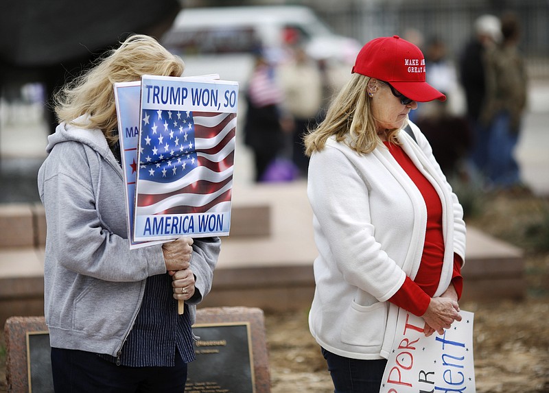Women bow their heads when an opening prayer is given at the start of the event. Many waving American flags and holding hand-made signs expressing pleasure with the new president, supporters of Donald Trump attended a rally Saturday, March 4, 2017, on the south plaza of the state Capitol in Oklahoma City to express their solidarity with him, his administration and his policies. (Jim Beckel/The Oklahoman via AP)