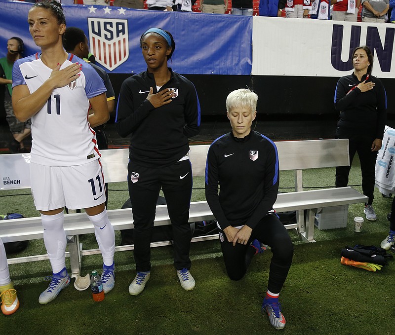 
              FILE - In this Sunday, Sept. 18, 2016 file photo, United States' Megan Rapinoe, right, kneels next to teammates Ali Krieger (11) and Crystal Dunn (16) as the U.S. national anthem is played before an exhibition soccer match against Netherlands in Atlanta. Megan Rapinoe says she will respect a new U.S. Soccer Federation policy that says national team players "shall stand respectfully" during national anthems. The policy was approved last month but came to light Saturday, March 4, 2017 before the U.S. women's national team lost to England in a SheBelieves Cup match. (AP Photo/John Bazemore, File)
            