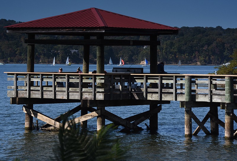 People relax on one of the fishing piers at Booker T. Washington State Park Sunday afternoon as the weekly sailboat race from Privateer Yacht Club gets underway on Chickamauga Lake.
