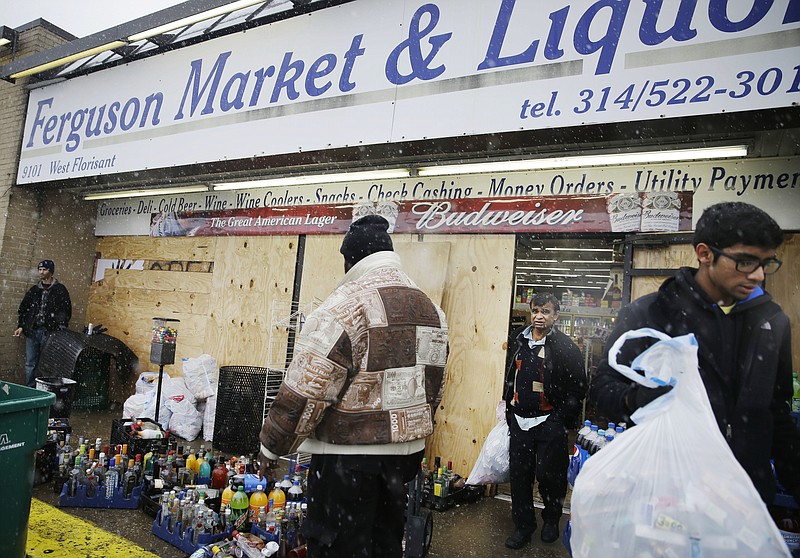 In this Wednesday, Nov. 26, 2014, file photo, Kush Patel, right, carries out bags of merchandise while helping his uncle Andy Patel, rear, clean up the looting damage from Monday's riots at his store, Ferguson Market and Liquor, in Ferguson, Mo. The store is disputing a new documentary's claims that surveillance video suggests Michael Brown didn't rob the store before he was fatally shot by police in Ferguson. One of the filmmakers said he believes the footage shows Brown trading marijuana for a bag of cigarillos early on Aug. 9, 2014, and that Brown intended to come back later for the cigarillos. Store officials said no drug transaction took place and Brown stole the cigarillos while at the store later that day. (AP Photo/David Goldman, File)