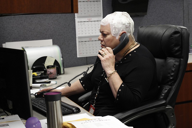 
              In this March 29, 2017 photo, Joyce Endresen wears an Optune therapy device for brain cancer, as she speaks on a phone at work in Aurora, Ill. She was diagnosed in December 2014 with Glioblastoma. She had two surgeries to remove the tumor as well as radiation and chemotherapy, but is now trying the new therapy that requires her to wear the electrodes on her head as much as possible. They create low intensity electric fields that disrupt cell reproduction, which makes the cells die. (AP Photo/Carrie Antlfinger)
            