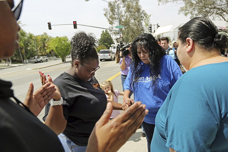 Marie Cabrera, second from right, leads a prayer group near a sidewalk memorial to the teacher and student who were shot to death Monday at North Park Elementary School in San Bernardino, Calif., Tuesday, April 11, 2017. (AP Photo/Reed Saxon)