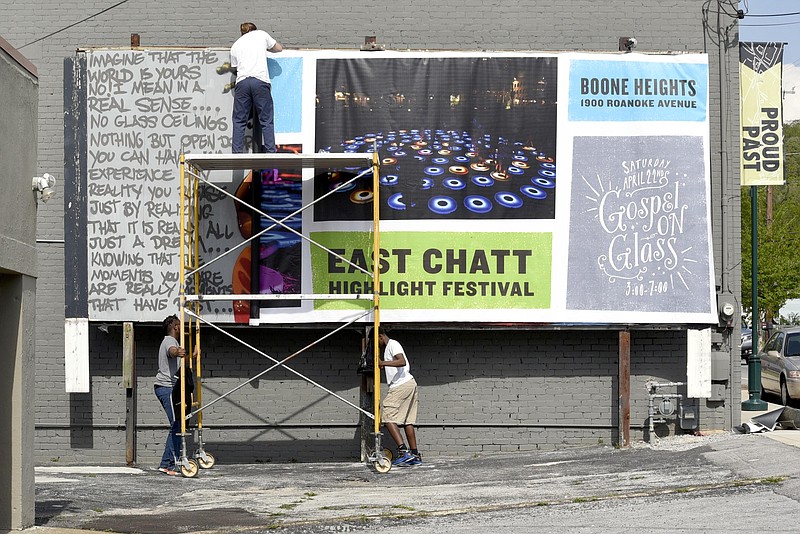 Chrystion McKibben, left, and Shemari McKibben move the scaffolding while Zack Atchley holds the sign in place. The Glass House Collective installed a billboard advertising its East Chatt Highlight Festival that starts Friday.