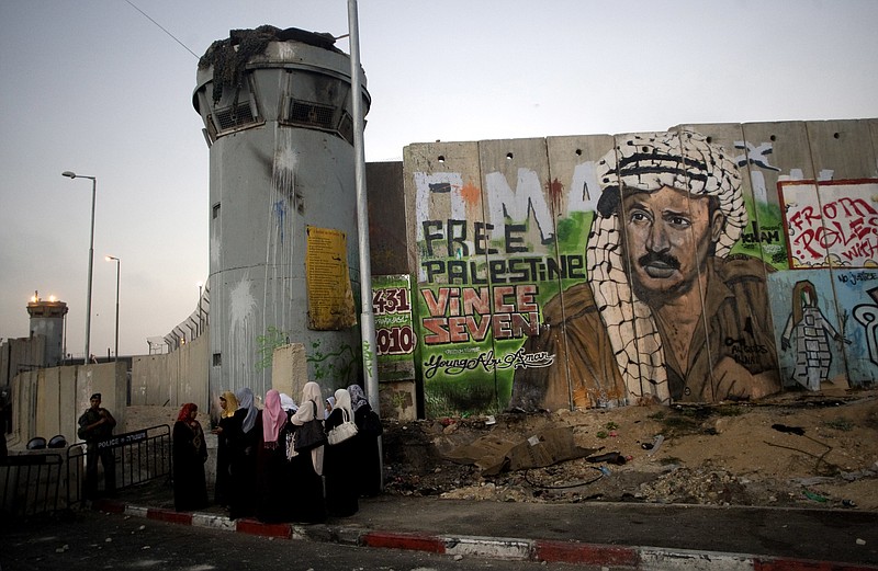 
              File - In this Friday, Aug. 13, 2010 file photo, Palestinian women wait near a section of Israel's separation barrier covered in graffiti, one depicting the late Palestinian leader Yasser Arafat, at the Qalandiya checkpoint , between Jerusalem and the West Bank city of Ramallah. Israel began construction of its 150-mile (250-kilometer) separation barrier in 2002 in response to a wave of Palestinian suicide bombings. Israel says the structure is a defense measure. But because it frequently juts into occupied West Bank land, the Palestinians see it as a land grab that poses an obstacle to their dream of establishing an independent state. (AP Photo/Sebastian Scheiner, File)
            