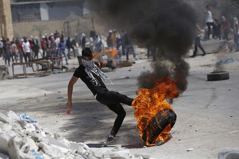 
              A Palestinian kicks a burning tire during clashes with Israeli forces following a rally in support of hunger-striking prisoners in Israeli jails, in the West Bank village of Beita, southeast of Nablus city, Friday, April 28, 2017. (AP Photo/Majdi Mohammed)
            