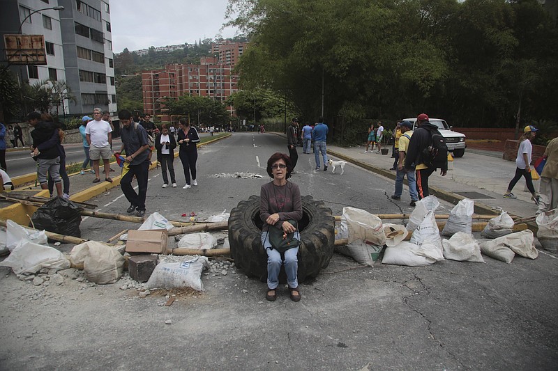 
              A woman rests on a tire at a roadblock set up by residents outside her home in El Hatillo's municipality near Caracas, Venezuela, Tuesday, May 2, 2017. Residents blocked streets with trash bags, broken concrete and twisted metal Tuesday to protest the president's bid to rewrite the constitution amid a deepening political crisis. (AP Photo/Fernando Llano)
            