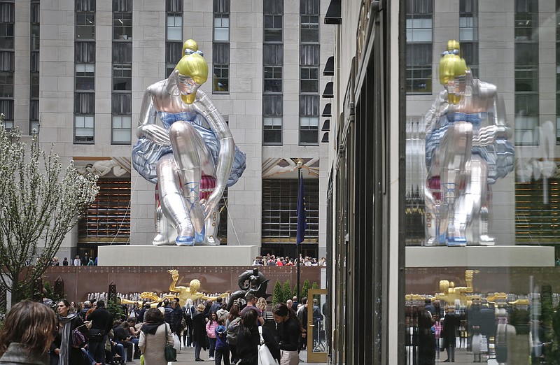
              "Seated Ballerina", center, the public art exhibition of a 45-foot tall inflatable nylon sculpture depicting a seated ballerina from artist Jeff Koons' Antiquity series, is displayed at Rockefeller Center after it was unveiled Friday May 12, 2017, in New York. (AP Photo/Bebeto Matthews).
            