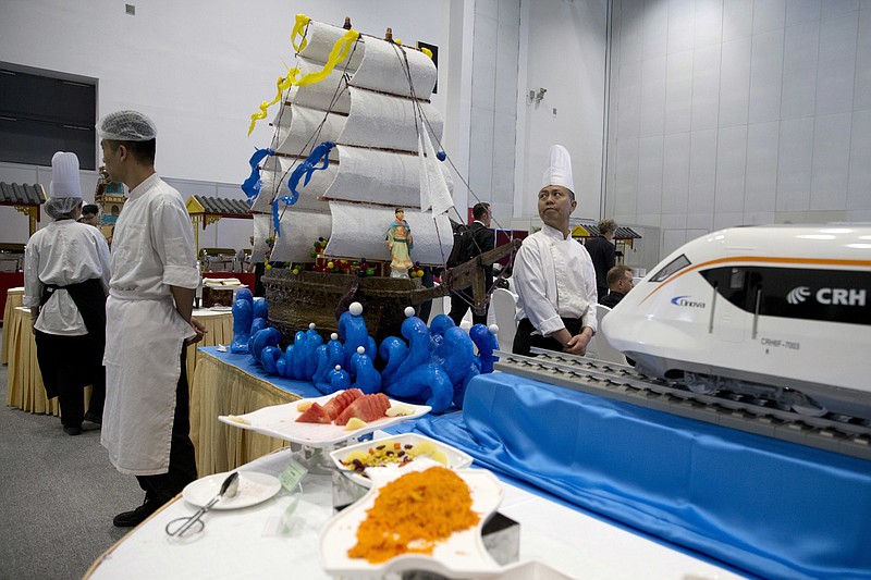 
              Chefs wait near a decorations depicting Chinese Admiral Zheng He who commanded expeditionary voyages across Asia and East Africa in the 15th century and a modern high speed rail at the Belt and Road Forum in Beijing, China, Sunday, May 14, 2017. China will seek to burnish President Xi Jinping's stature as a world-class statesman at the international gathering centered on his signature foreign policy effort that envisions a future world order in which all roads lead to Beijing. (AP Photo/Ng Han Guan)
            