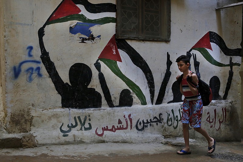 
              In this Thursday, May 4, 2017 photo, a boy walks by graffiti of the Palestinian flags with Arabic reads: "The flag is four colors that shine on the face of the sun" in the Bourj al-Barajneh Palestinian refugee camp in Beirut, Lebanon. On Monday, Palestinians mark 69 years since hundreds of thousands of them were forced from their homes during the 1948 war that led to the creation of Israel. Palestinians in Lebanon suffer discrimination in nearly every aspect of daily life, feeding a desperation that is tearing their community apart. (AP Photo/Bilal Hussein)
            