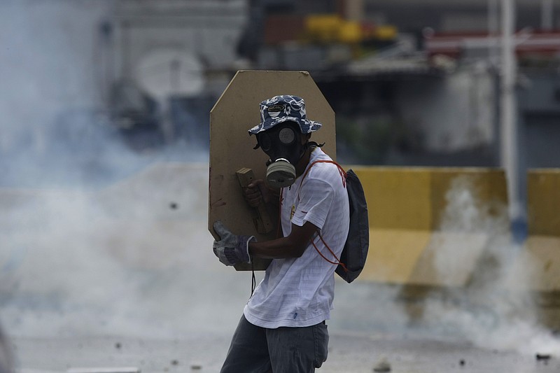 
              A masked anti-government protester shields himself during clashes with security forces, in Caracas, Venezuela, Thursday, May 18, 2017. The protest in Caracas comes after a tumultuous 24 hours of looting and protests in the western state of Tachira that led the government to send in troop reinforcements. More than 40 people have been killed in almost two months of unrest in Venezuela. (AP Photo/Fernando Llano)
            