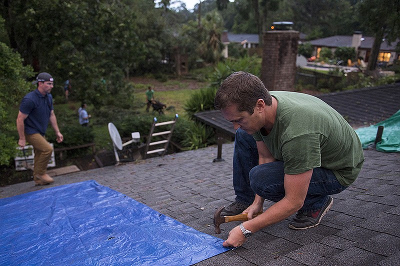 
              Hunter Saussy the IV hammers in nails to hold a tarp in place over a hole in his friend's roof on Wilmington Island, Ga., after a severe storm passed through the area causing heavy damage to several houses Tuesday evening, May 23, 2017. The threat of flooding continues across several southern states as heavy rain soaked the area and prompted new flood watches in the Carolinas while a massive storm system swept eastward. (Josh Galemore/Savannah Morning News via AP)
            