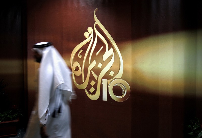 
              FILE -- In this Nov. 1, 2006 file photo, a Qatari employee of Al Jazeera Arabic language TV news channel walks past the logo of Al Jazeera in Doha, Qatar. Hackers allegedly broke into the website of Qatar's state-run news agency and published a fake story quoting the ruling emir, authorities there said Wednesday, May 24, 2017, as Saudi Arabia and the United Arab Emirates responded by blocking Qatari media, including broadcaster Al-Jazeera. (AP Photo/Kamran Jebreili, File)
            