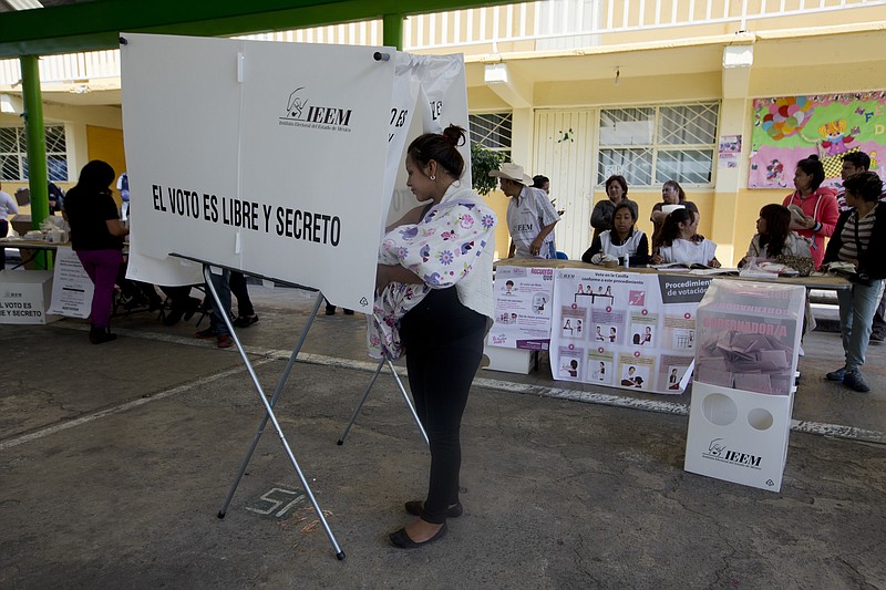 A woman holding a child fills out her ballot in a privacy booth during gubernatorial elections for Mexico State, in Ecatepec, Mexico, Sunday, June 4, 2017. Voters in Mexico's most populous state on Sunday could hand the ruling PRI party a much-needed boost ahead of next year's presidential elections or a potentially devastating blow by throwing off its uninterrupted 88-year local rule. (AP Photo/Eduardo Verdugo)