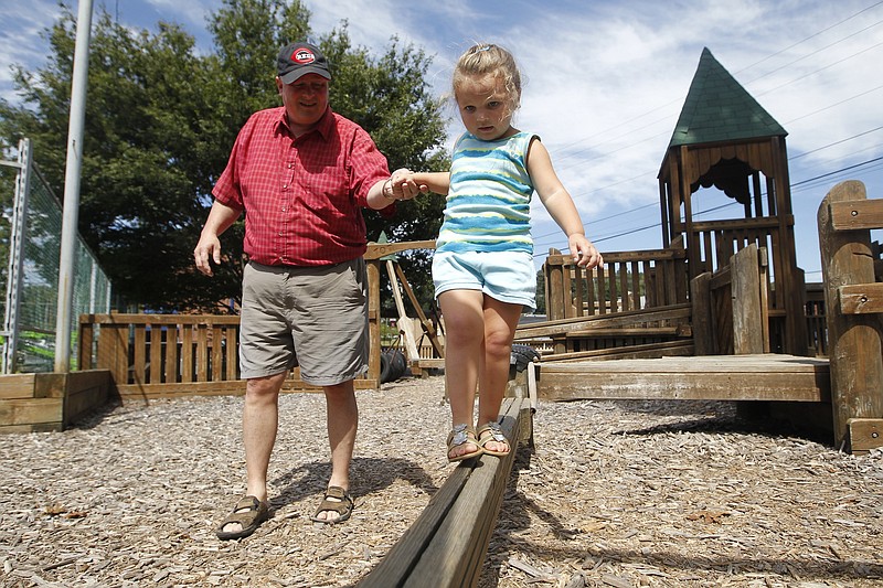 Greg Matthew helps his granddaughter Harper, 3, walk across a balance beam at the Kids Korner playground in this 2014 photo. (Staff file photo)