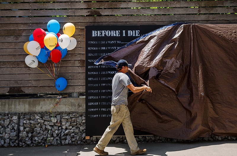 Mike Wayne unveils a "Before I Die" art wall in Coolidge Park beneath the Chief John Ross Bridge on Tuesday, June 20, 2017, in Chattanooga, Tenn. The wall, sponsored by Hospice of Chattanooga, allows visitors to leave messages detailing what they want to do before they die.
