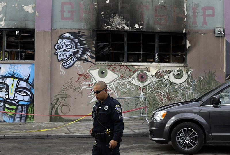 
              File - In this Dec. 9, 2016 file photo, an Oakland police officer guards the area in front of the art collective warehouse known as the Ghost Ship in the aftermath of a fire in Oakland, Calif. More than six months after the Dec. 2 blaze at the warehouse that authorities said was illegally converted into living quarters, the Oakland Fire Department has released a 50-page report filled with harrowing details of death and panic as the flames and deadly smoke spread. The report contains many previously unknown details about the nation's deadliest structure fire in more than 14 years and says investigators could not determine the cause of the blaze due to extensive fire damage.(AP Photo/Ben Margot)
            