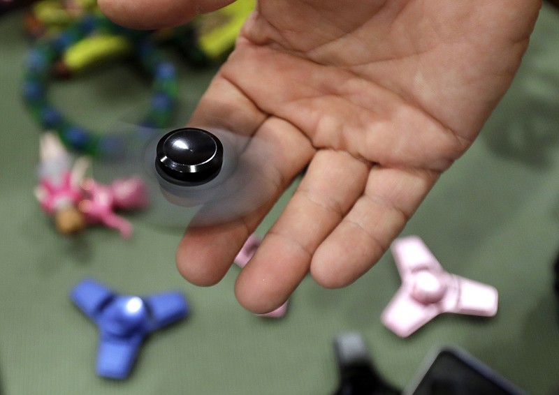 
              FILE - In this May 11, 2017, file photo, Funky Monkey Toys store owner Tom Jones plays with a fidget spinner in Oxford, Mich. Fidget spinners are among the those on the annual list of hazardous summer toys compiled by World Against Toys Causing Harm, Inc., a nonprofit consumer watchdog. (AP Photo/Carlos Osorio, File)
            