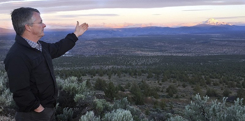 
              Joe Krenowicz, executive director of the Madras-Jefferson County Chamber of Commerce, gestures toward Mt. Jefferson as the sun rises over Madras, Oregon on June 13, 2017. The first place to experience total darkness as the moon passes between the sun and the Earth will be in Oregon and Madras, in the central part of the state, is expected to be a prime viewing location. Up to 1 million people are expected in Oregon for the first coast-to-coast total solar eclipse in 99 years and up to 100,000 could show up in Madras and surrounding Jefferson County. Officials are worried about the ability of the rural area to host so many visitors and are concerned about the danger of wildfire from so many people camping on public lands. (AP Photo/Gillian Flaccus)
            