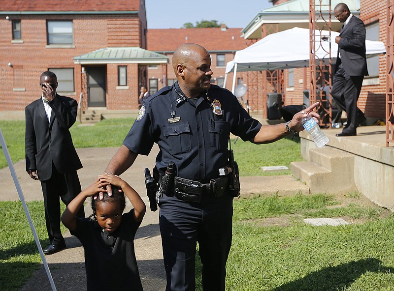 Chattanooga Police Captain Edwin McPherson puts his hand on the head of Dominique Collins as he waves to people while arriving Saturday, Aug. 16, 2014, at a stop the violence community picnic at East Lake Courts in Chattanooga, Tenn. The picnic offered food, music, and a chance for kids to tour police squad cars and fire engines.