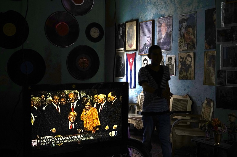 
              FILE - In this June 16, 2017, file photo, a man walks past a television set showing U.S. President Donald Trump signing the new Cuba policy, in a living room festooned with images of Cuban leaders at a house in Havana, Cuba. President Trump declared he was restoring some travel and economic restrictions on Cuba that were lifted as part of the Obama administration's historic easing. (AP Photo/Ramon Espinosa, File)
            