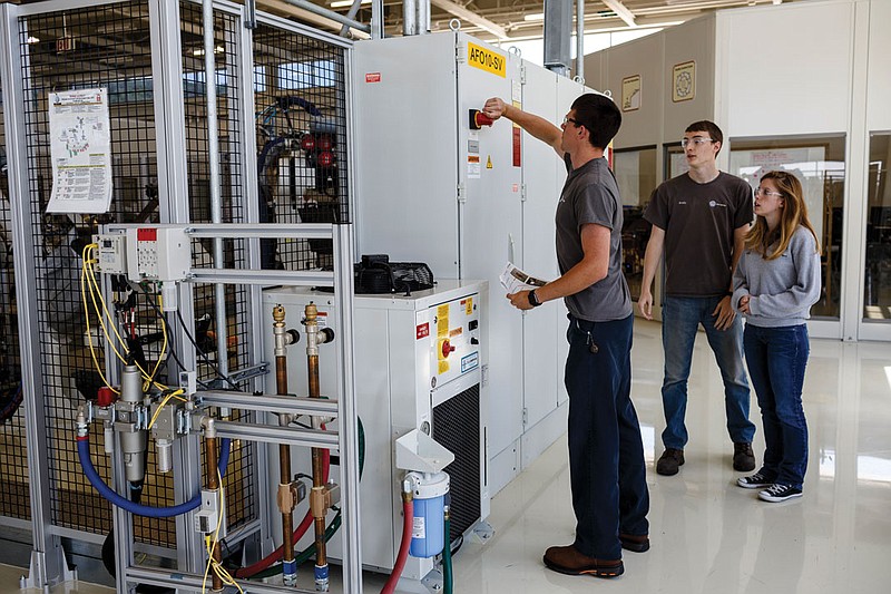 Mechatronics students Aaron English, left, and Brady Crews, center, demonstrate the operation of a robot with supervision from EST 3 engineer Shelby Dreifke at the Volkswagen Academy.