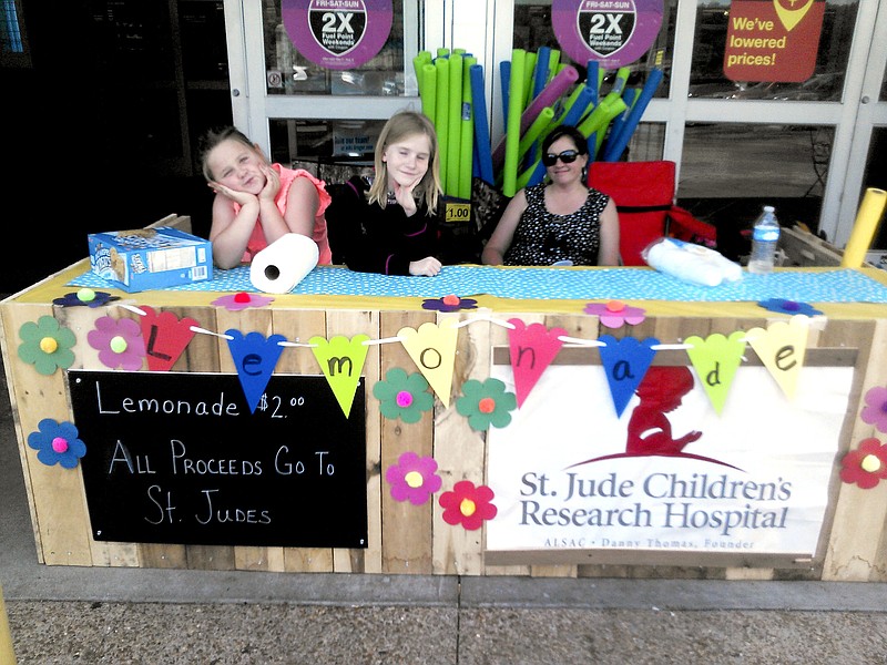 Caption: Kelsi Goins, left, and her friend Elie Mae Fletcher, center, wait for customers at their lemonade stand in Harriman, Tenn., earlier this month. Kelsi's mother, Melissa Goins, right, supervises the operation. 