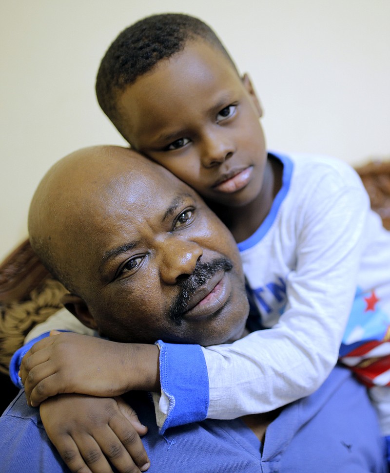 
              Sudanese activist Tayeb Ibrahim, who had worked to expose Sudanese abuses in the volatile South Kordofan province and hopes to see family living in the U.S. state of Iowa, is hugged by his son Mohammed during an interview with The Associated Press in Cairo, Egypt, Wednesday, June 28, 2017. Dozens of Sudanese activists living in Egypt as refugees, many of whom fled fundamentalist Islamic militias and were close to approval for resettlement in the United States, now face legal limbo in Egypt after the Supreme Court partially reinstated President Donald Trump's travel ban. (AP Photo/Amr Nabil)
            