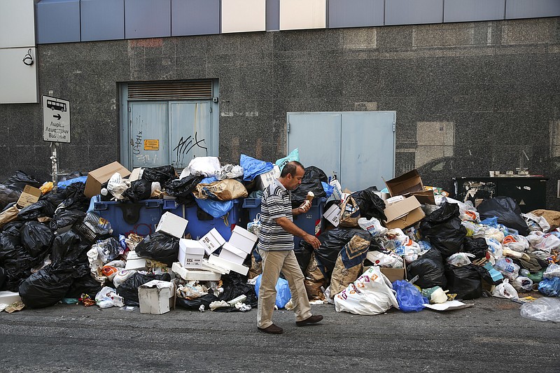 
              A man holds an ice cream as he makes his way past a pile of garbage in Athens, on Thursday, June 29, 2017. A strike by garbage collectors, which has lasted nearly two weeks, has left towering mounds of garbage on city streets at a time when the summer's first heatwave sent temperatures soaring. (AP Photo/Yorgos Karahalis)
            