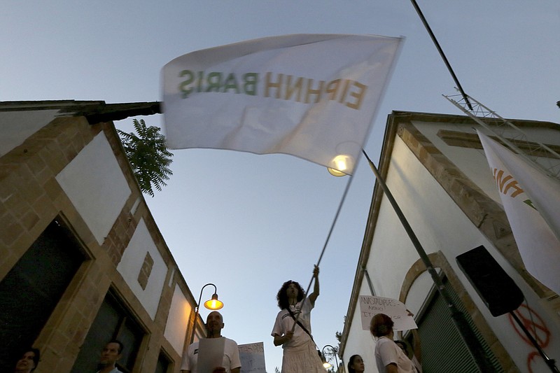 
              A supporter for peace waves a flag reading in Greek and Turkish "Peace" during a protest with Greek and Turkish Cypriots to call to the rival leaders of the two communities for a peace in the island at Ledras main crossing point inside the U.N buffer zone that divided the Greek and Turkish Cypriots controlled areas, Nicosia, Cyprus, Wednesday, June 28, 2017. Several hundred Greek Cypriots and Turkish Cypriots gathered in the divided capital's medieval center at a checkpoint along the U.N.-controlled buffer zone to voice their support for peace. (AP Photo/Petros Karadjias)
            