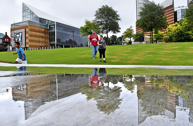 A puddle atop the Riverpark's terraced steps reflects the Tennessee Aquarium's spires as the Lucas Family, from left, Henry, J.J. and Monica, of Nashville, walk down to the Tennessee River between showers on June 30. 2017.  The Chattanooga area has experienced a rainy Summer so far this season.  