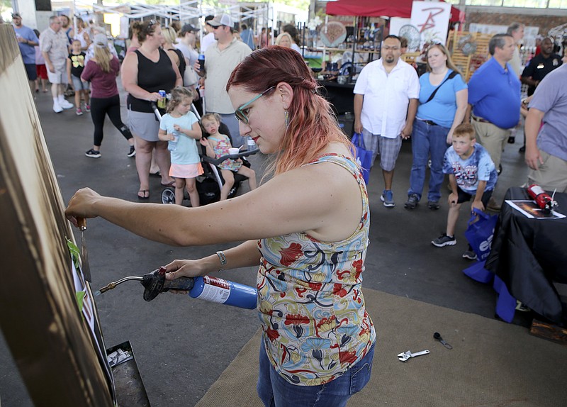 People look on as Hollie Berry works on a torch painting during the Local Artists Festival at the Chattanooga Market at the First Tennessee Pavilion on Sunday, July 16, in Chattanooga, Tenn. Local artists shared and sold their work at the market. Berry was one of the featured artists.