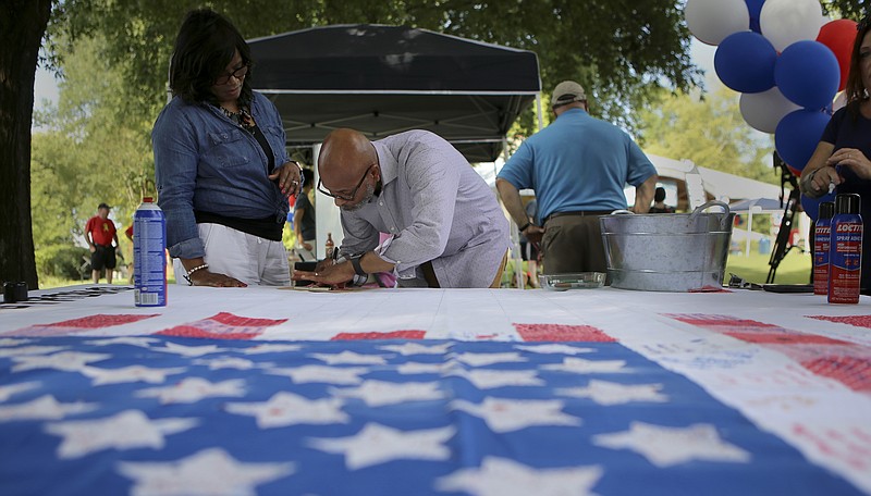 As his wife Sabrina looks on, Tony Sammons writes on a square that will be put into a stripe on an American flag during the Chattanooga Strong Community Concert at the Hubert Fry Center in the Tennessee Riverpark on Sunday, July 16, in Chattanooga, Tenn. People wrote inspirational messages on red or white squares which were then attached to the large American flag to make up the stripes.