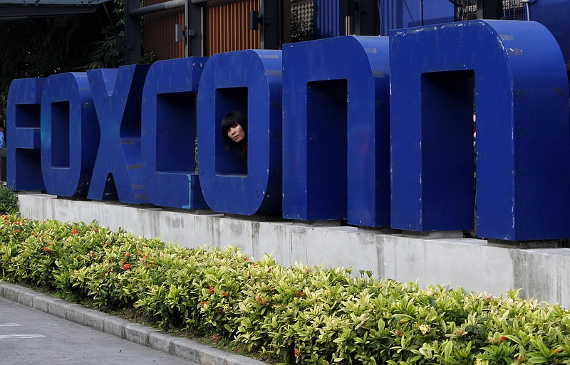 
              FILE - In this Thursday, May 27, 2010, file photo, a worker looks out through the logo at the entrance of the Foxconn complex in the southern Chinese city of Shenzhen. Taiwanese electronics maker Foxconn's plan to build a display panel factory in the U.S. has sparked a flurry of lobbying by states vying to land what some economic development officials say is a once-in-a-generation prize. (AP Photo/Kin Cheung, File)
            