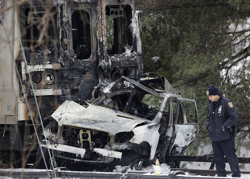 
              FILE- In this Feb. 4, 2015, file photo, a police officer looks at an SUV that was crushed at the front of a Metro-North Railroad train in Valhalla, N.Y. Federal investigators have concluded that a fiery crash between a commuter train and an SUV that killed six people in the suburbs in 2015 was extra deadly because of an unusual rail design, a U.S. official told The Associated Press on Monday, July 24, 2017. (AP Photo/Mark Lennihan, File)
            